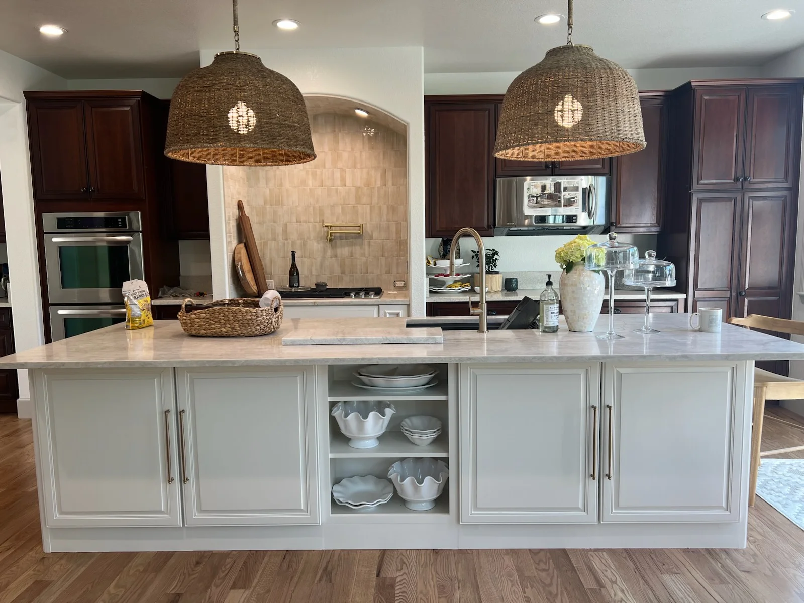 Modern kitchen with white cabinetry, quartz island, stainless appliances, and woven pendant lights