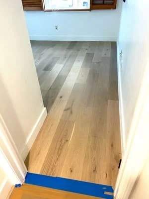 Newly installed hardwood flooring in hallway with mixed wood tones and protective tape