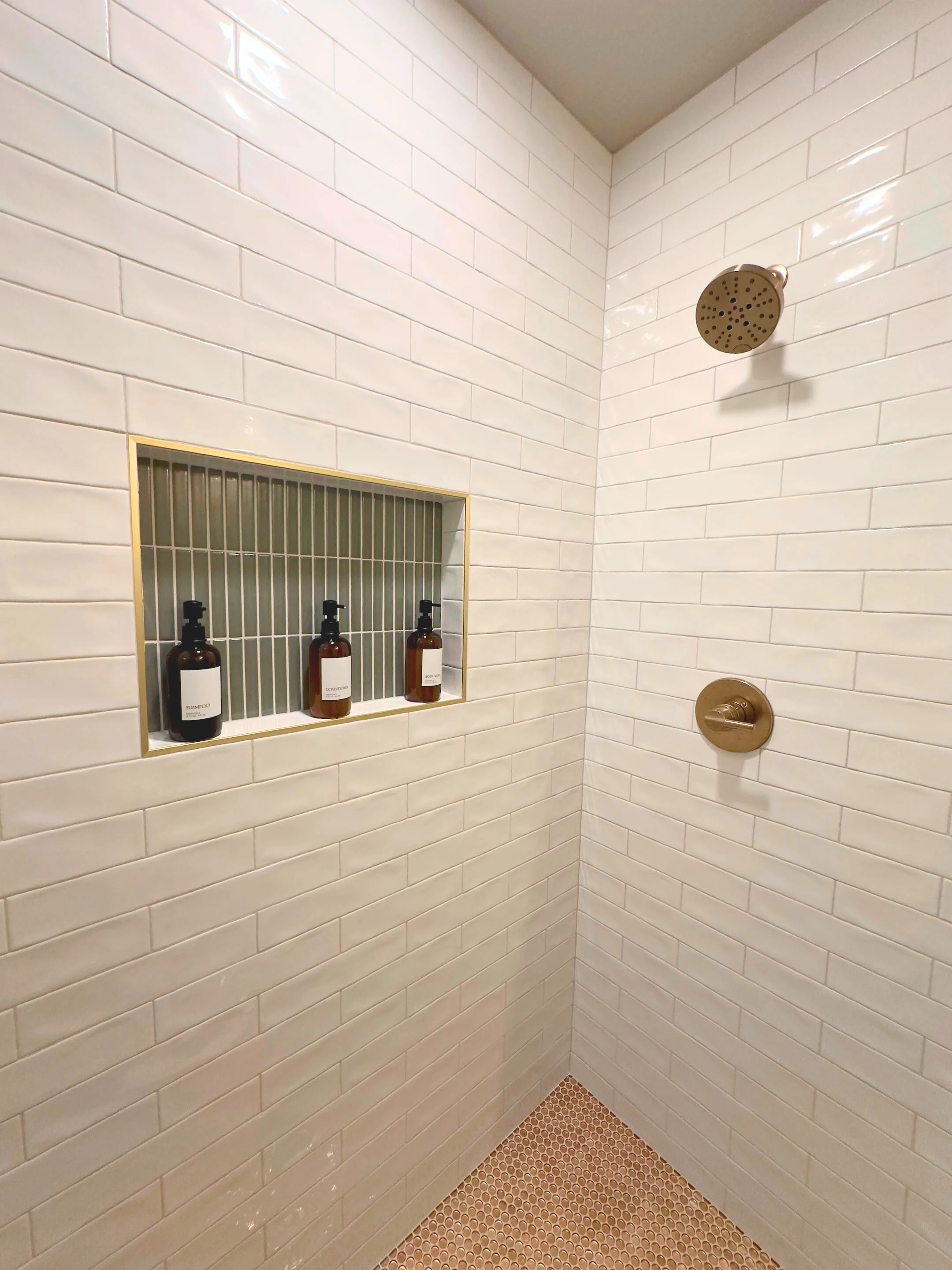 White subway tile shower with brass niche, bronze fixtures, and hexagonal floor tile
