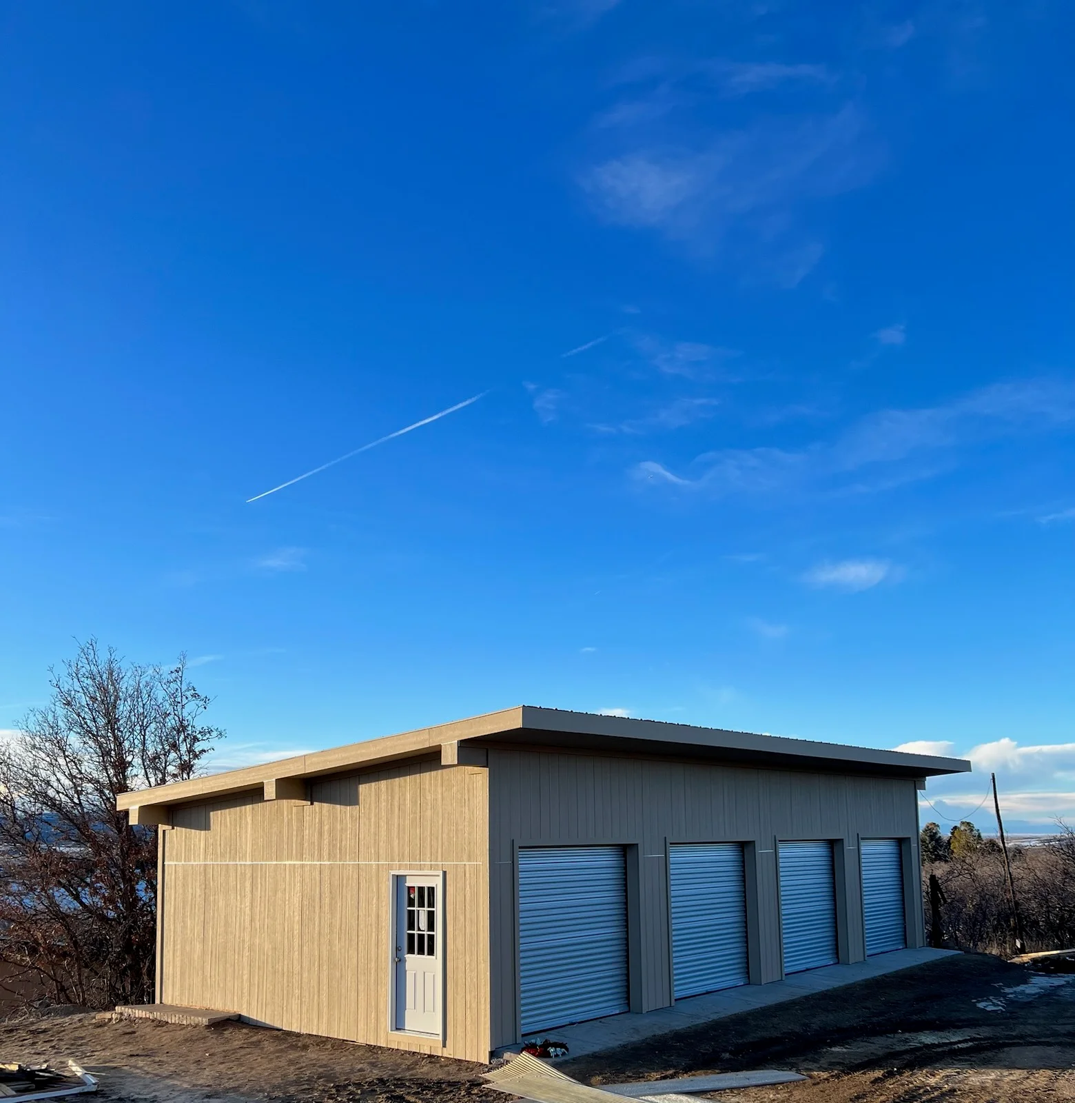 Modern storage building with wood and metal siding, four blue roll-up garage doors