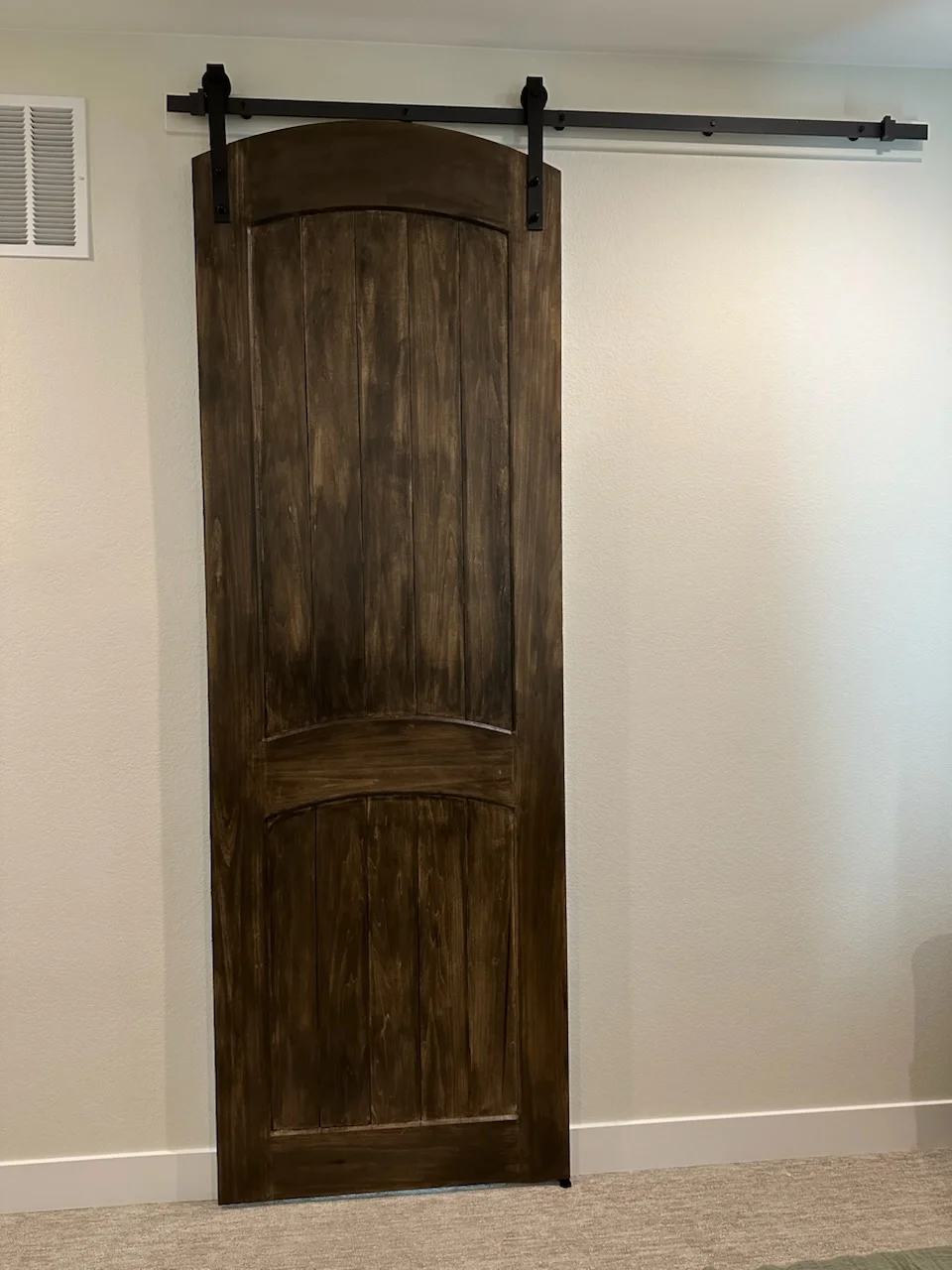 Dark wood barn door with curved panels and black steel sliding hardware mounted on interior wall