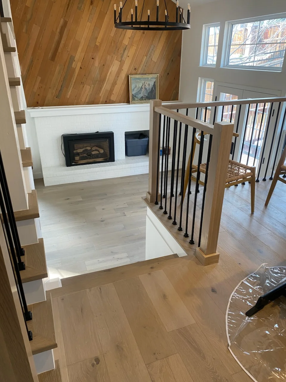Open loft space with white shiplap fireplace, hardwood floors, wood and metal stair railing