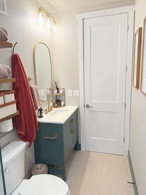 Renovated bathroom with teal vanity, brass mirror, white door, and updated fixtures