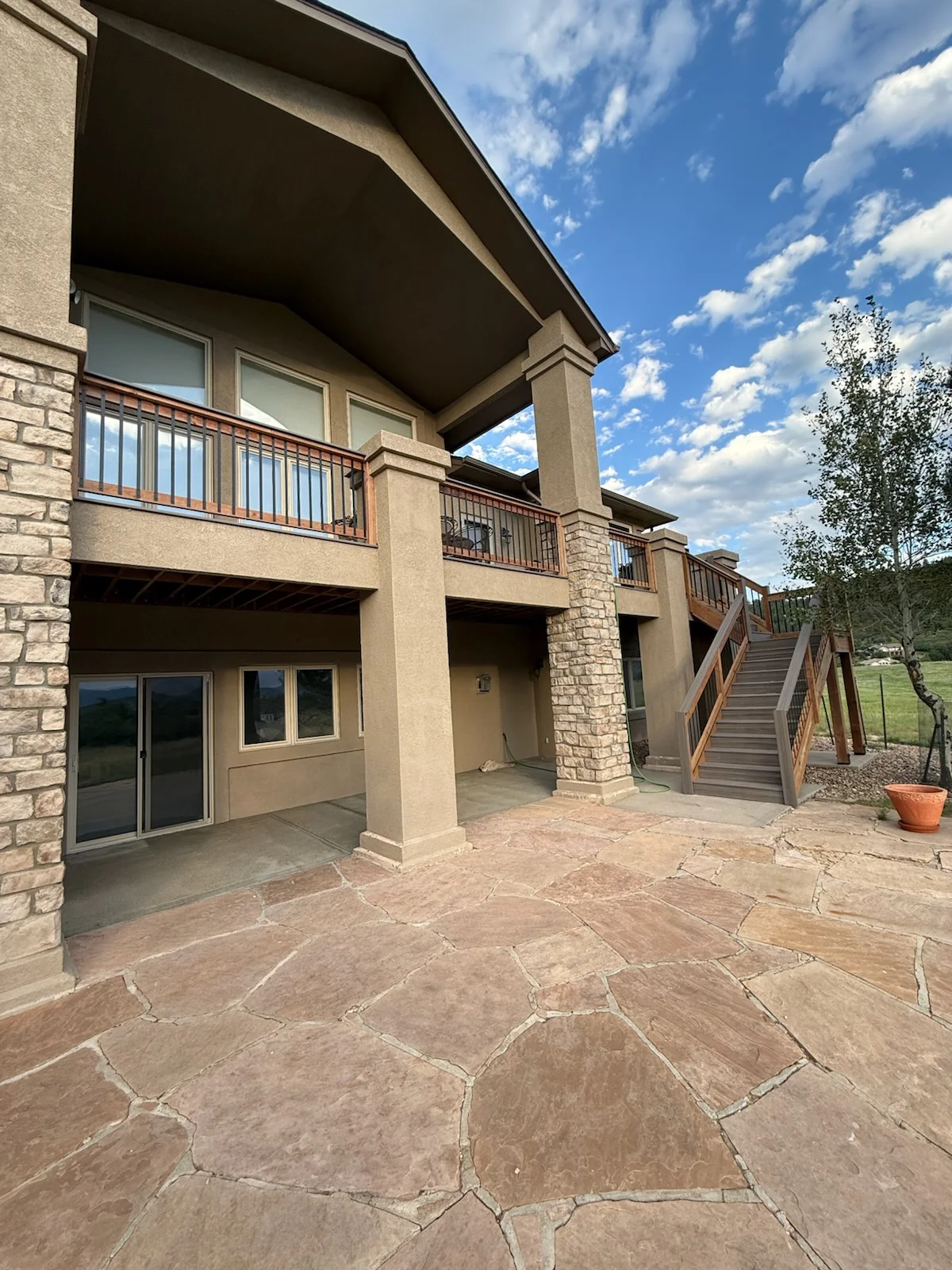 Flagstone patio with composite deck, metal railings, and wooden stairs on multi-level exterior
