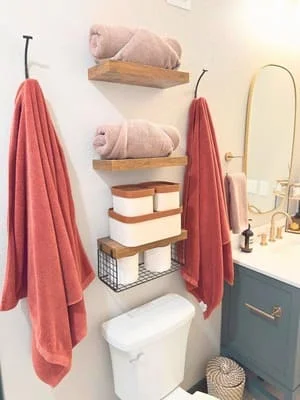 Renovated bathroom with floating wood shelves, red towels, white toilet, and gold-trimmed vanity mirror