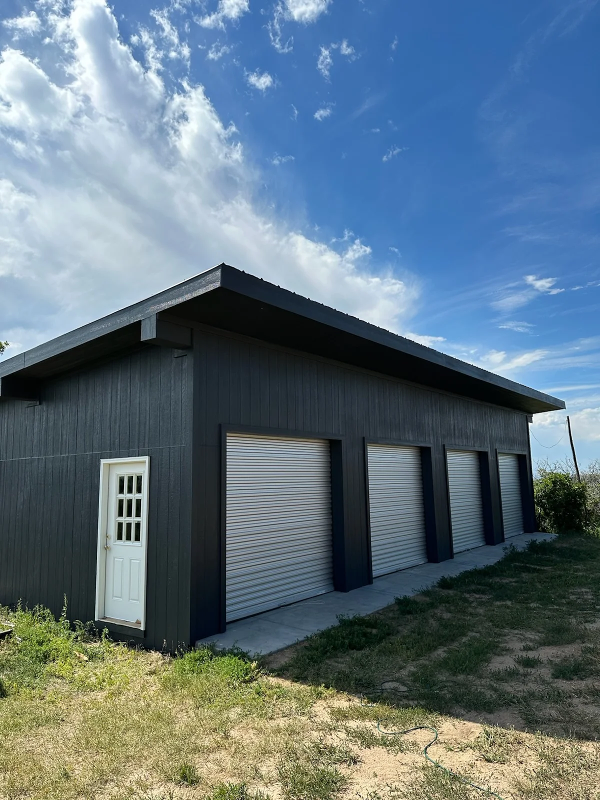 Dark metal garage with three roll-up doors, corrugated steel siding, and concrete foundation