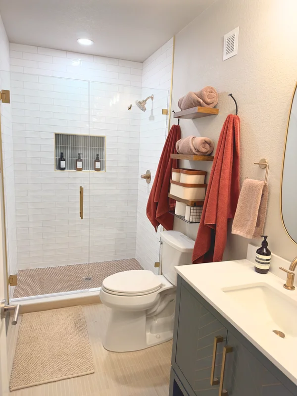 Renovated bathroom with glass shower enclosure, white subway tile, floating shelves, and gray vanity