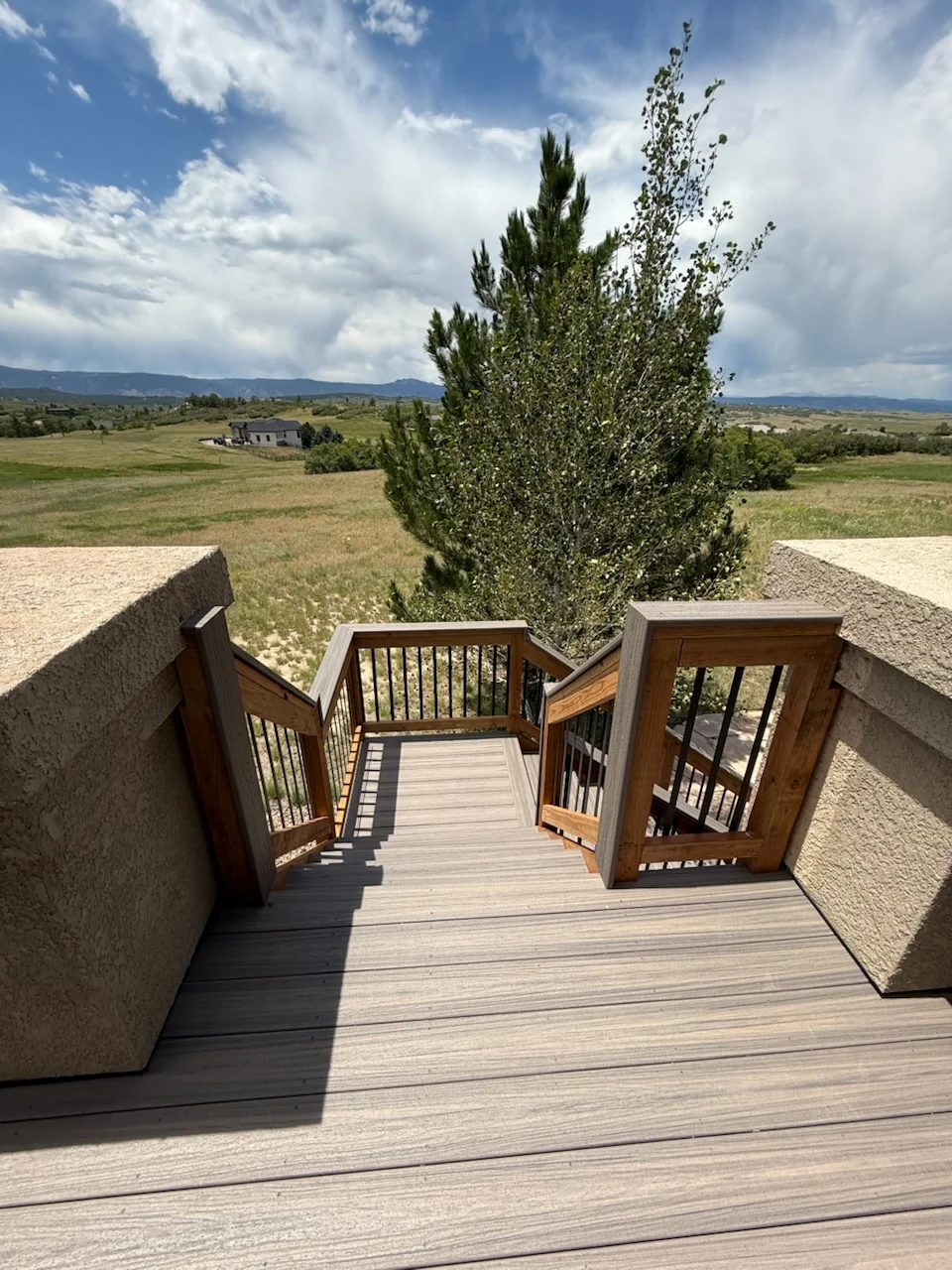 Composite deck with stone walls, wooden gates, and metal railings overlooking rural landscape