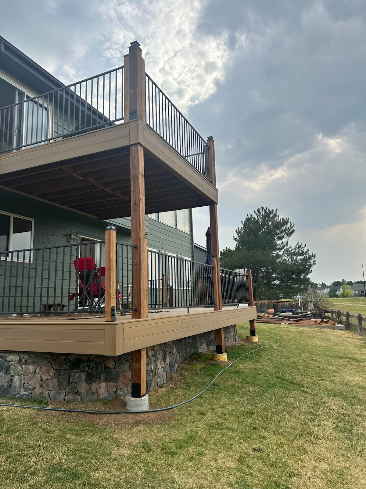 Two-story composite deck with black railings, wood posts, and stone foundation base