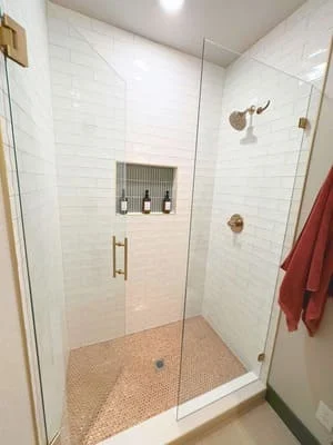 Modern walk-in shower with frameless glass doors, white subway tile, and terra cotta floor