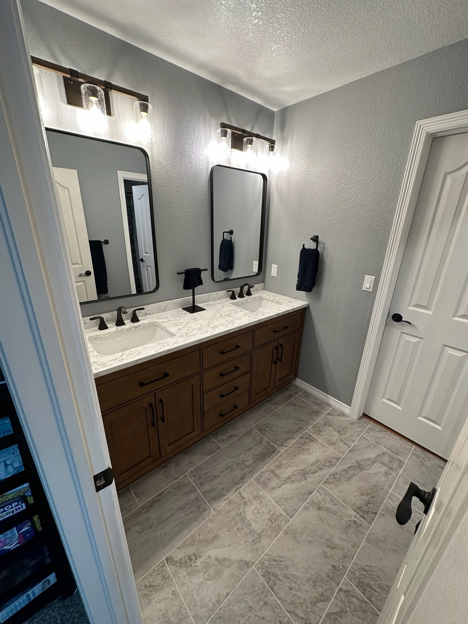 Master bathroom with dark wood double vanity, marble countertop, dual mirrors, and tile flooring