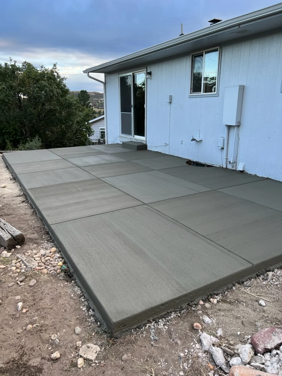 Finished concrete patio with broom texture and control joints next to white residential home