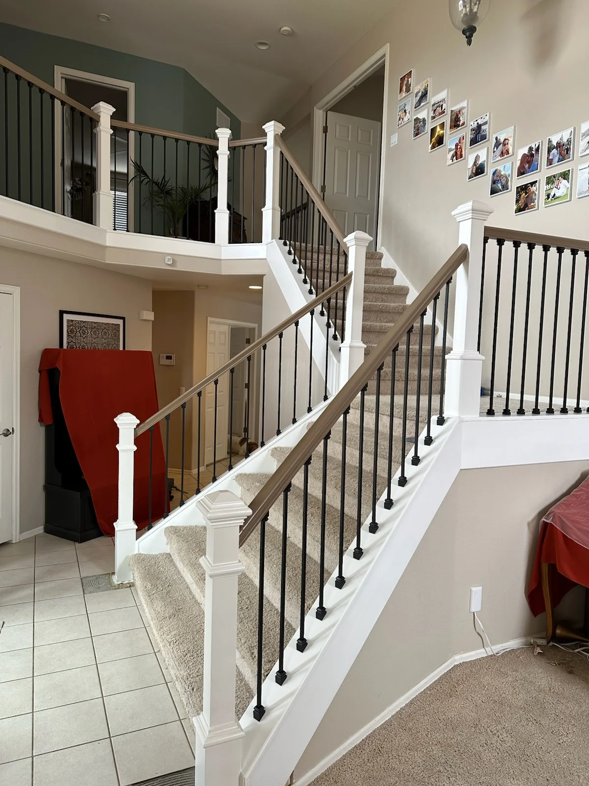 Two-story staircase with white newel posts, wood handrail, black metal balusters, and carpet treads