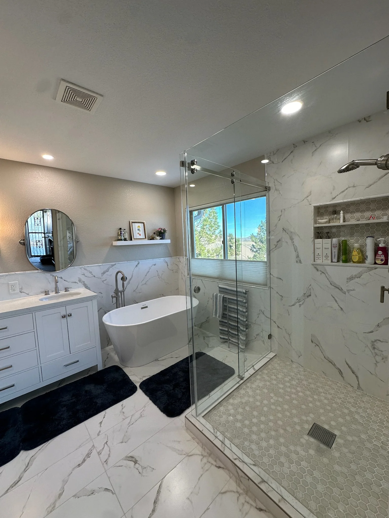 Modern bathroom with marble tile, freestanding tub, frameless glass shower, white cabinetry, and recessed lighting