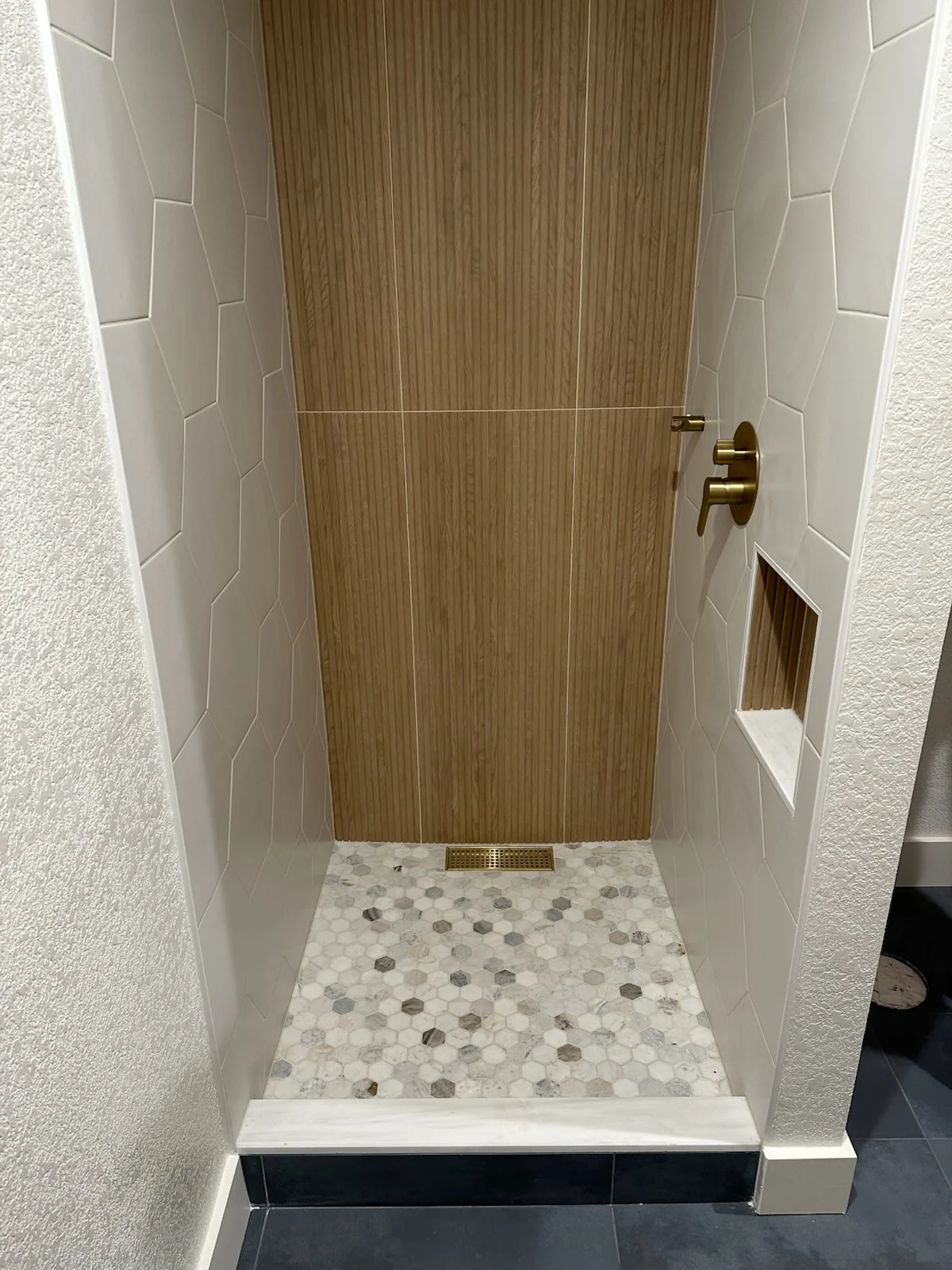 Shower stall with wood-grain tile, white subway tile walls, and marble hexagon floor mosaic