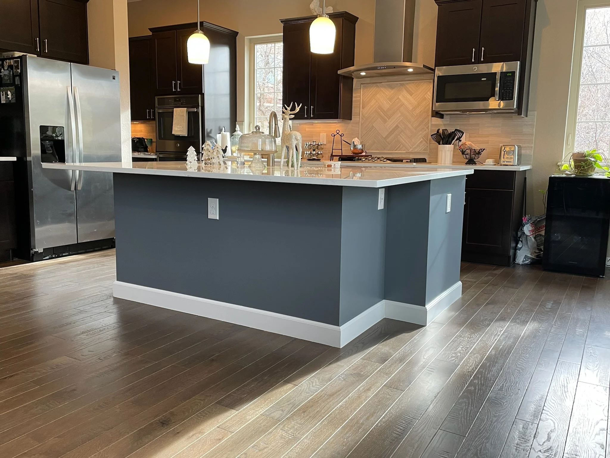 Modern kitchen with dark cabinets, gray island, quartz counters, and wood-look flooring