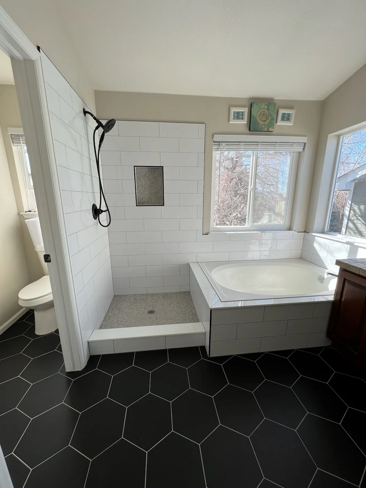 Master bathroom with white subway tile shower, black hexagonal floor tile, soaking tub, and updated fixtures