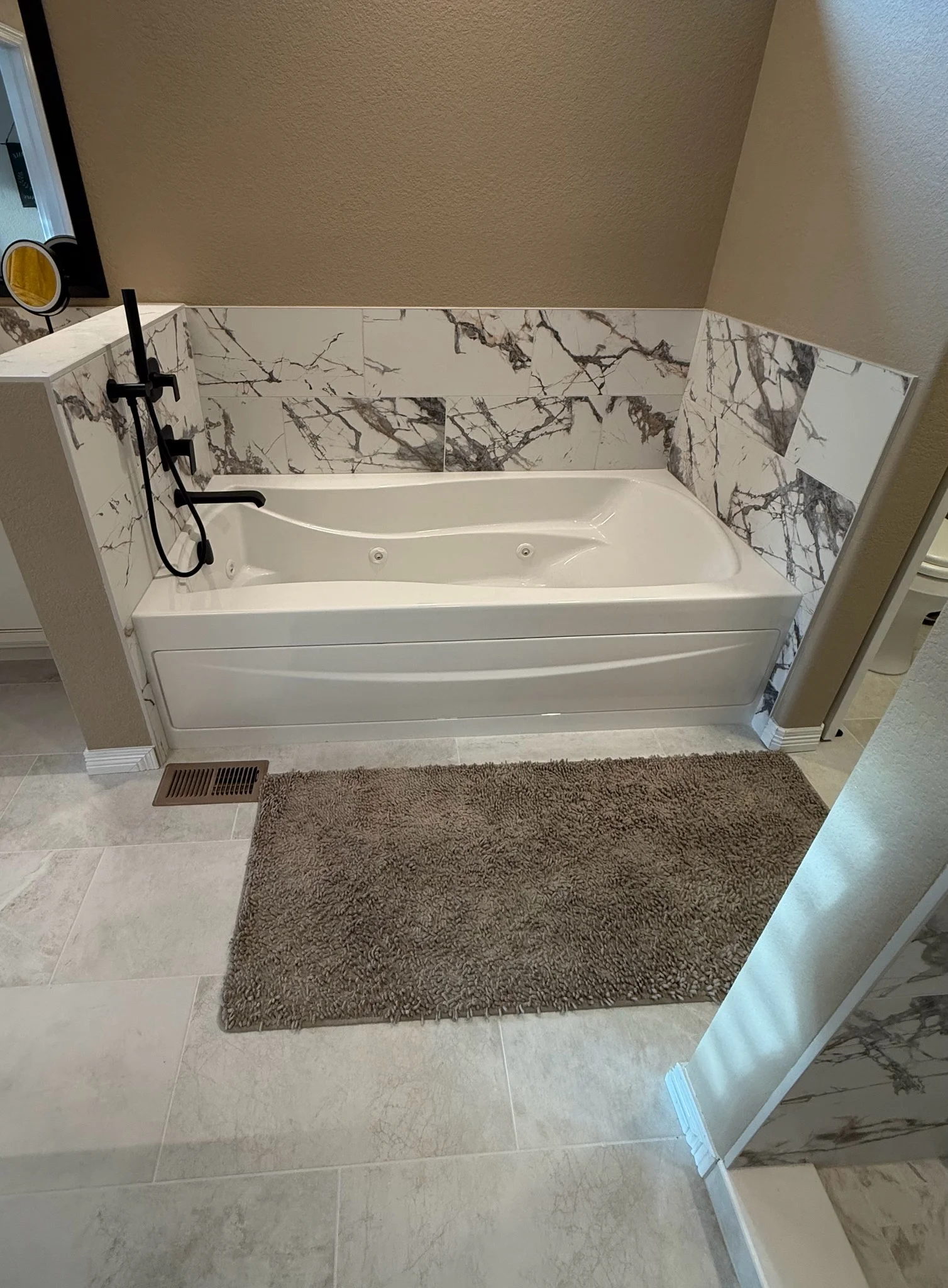 White soaking tub with black faucet, marble tile surround, and gray porcelain floor tile in bathroom