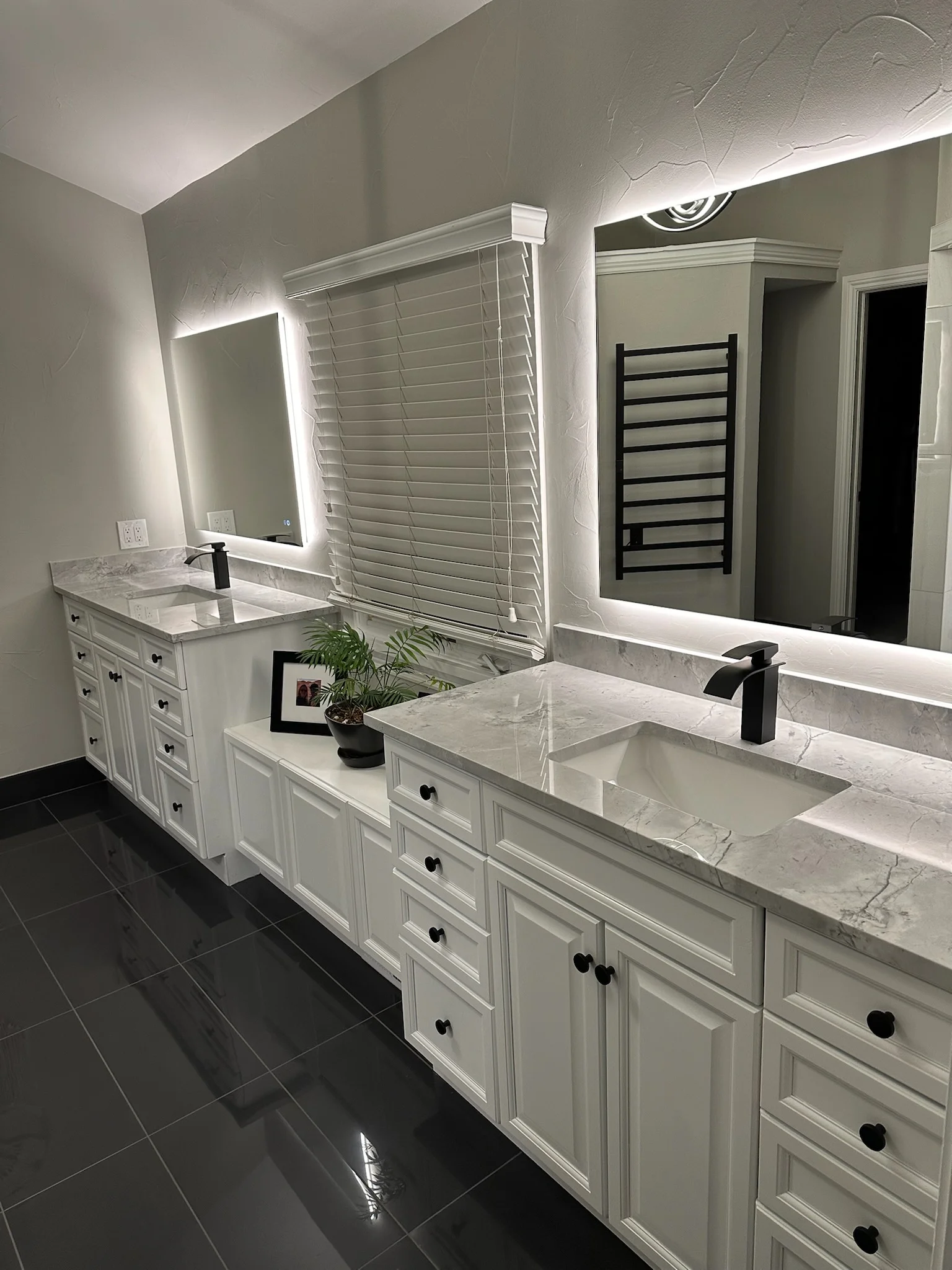 Dual vanity bathroom with white cabinetry, marble countertops, LED mirrors, black tile flooring