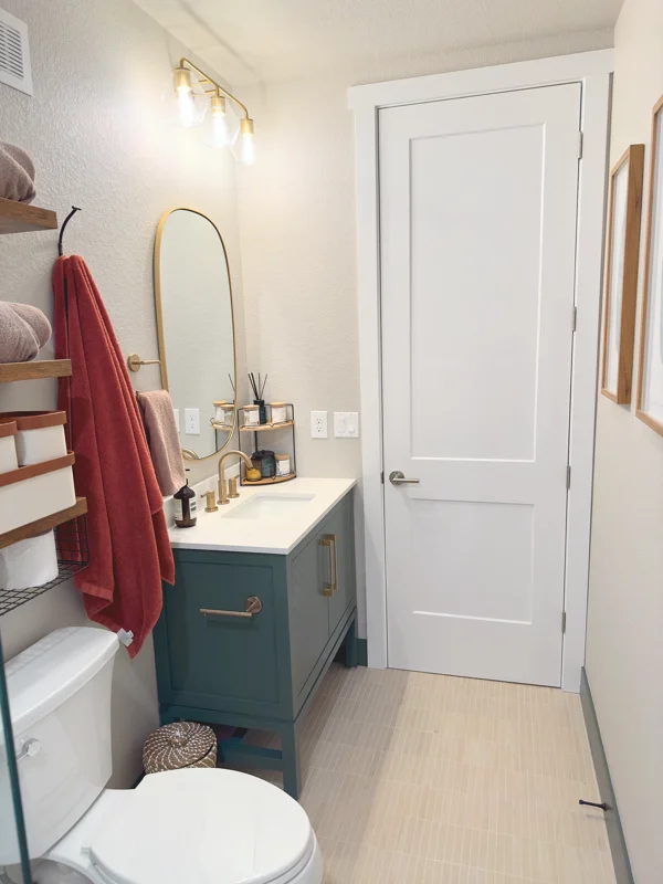 Bathroom with teal vanity, white quartz countertop, brass fixtures, and vinyl plank flooring