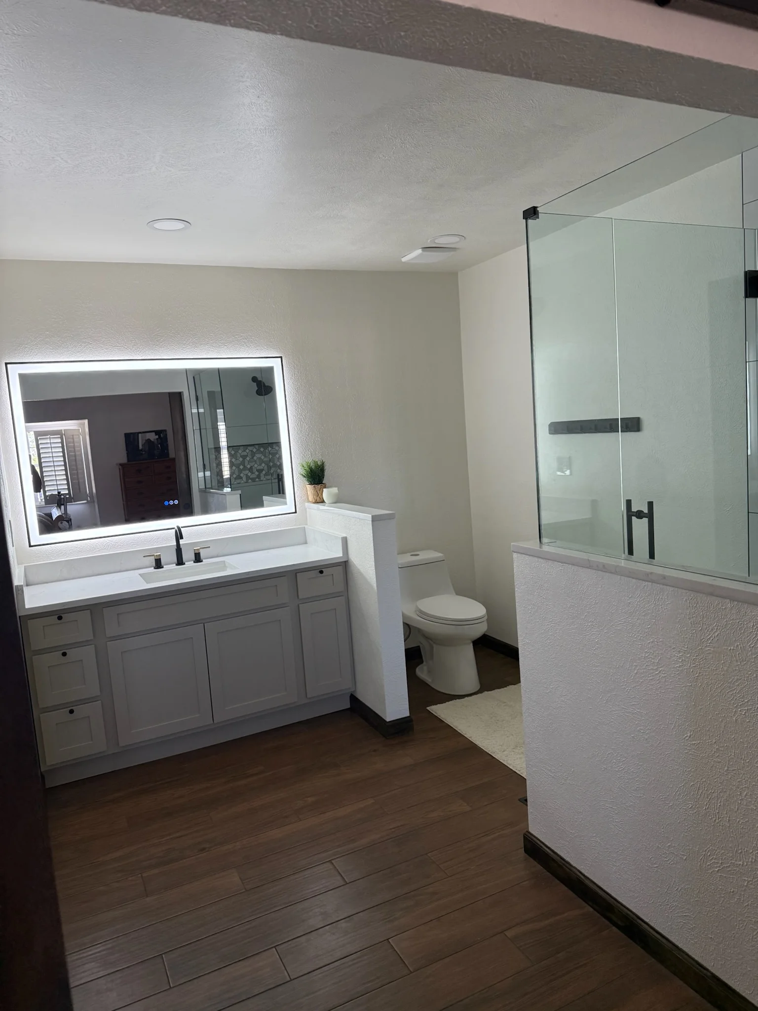 Bathroom with gray vanity, LED mirror, frameless glass shower, and wood flooring