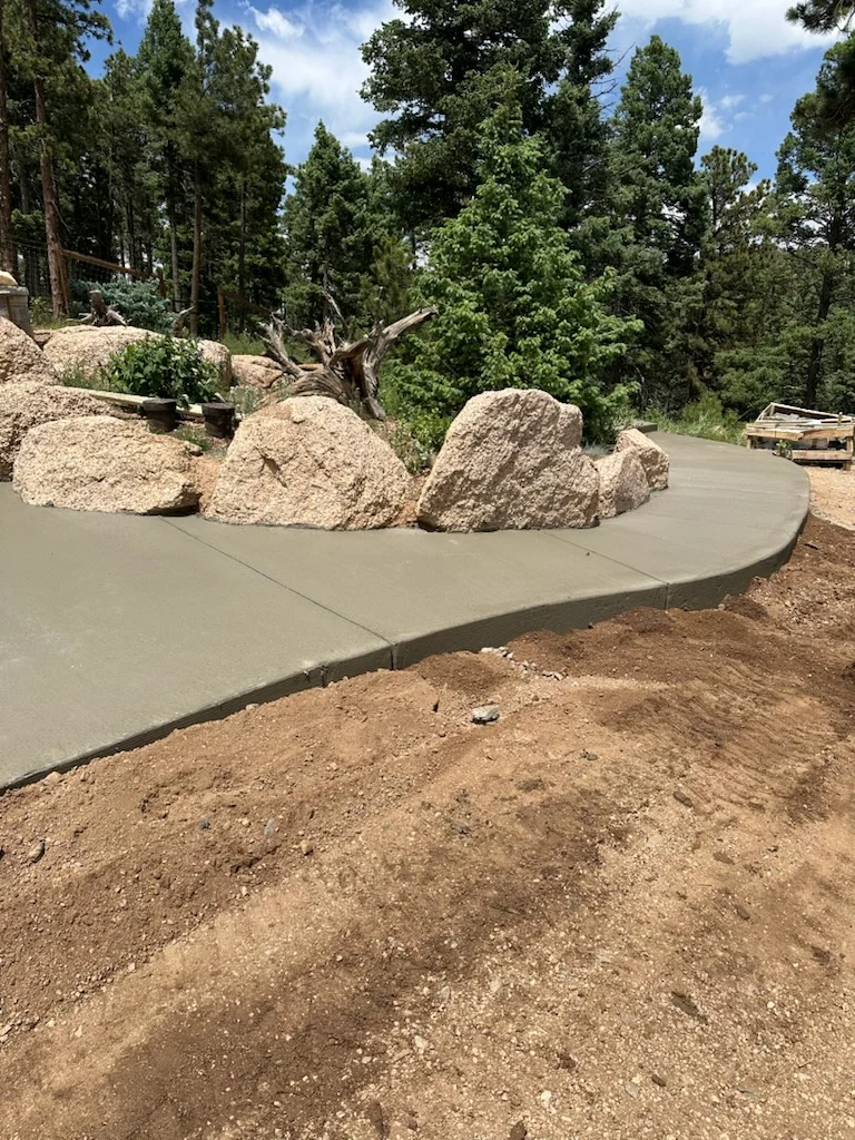 Curved concrete patio with large boulders and forest backdrop