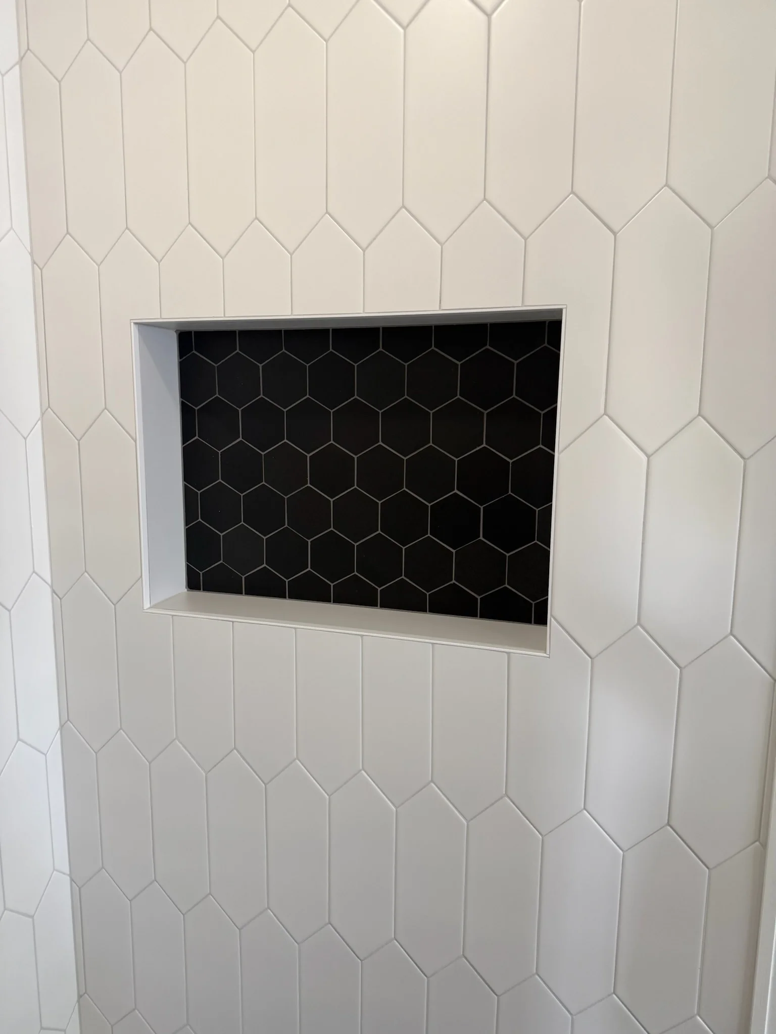 White hexagonal tile shower wall with recessed niche and black hexagonal mosaic backing