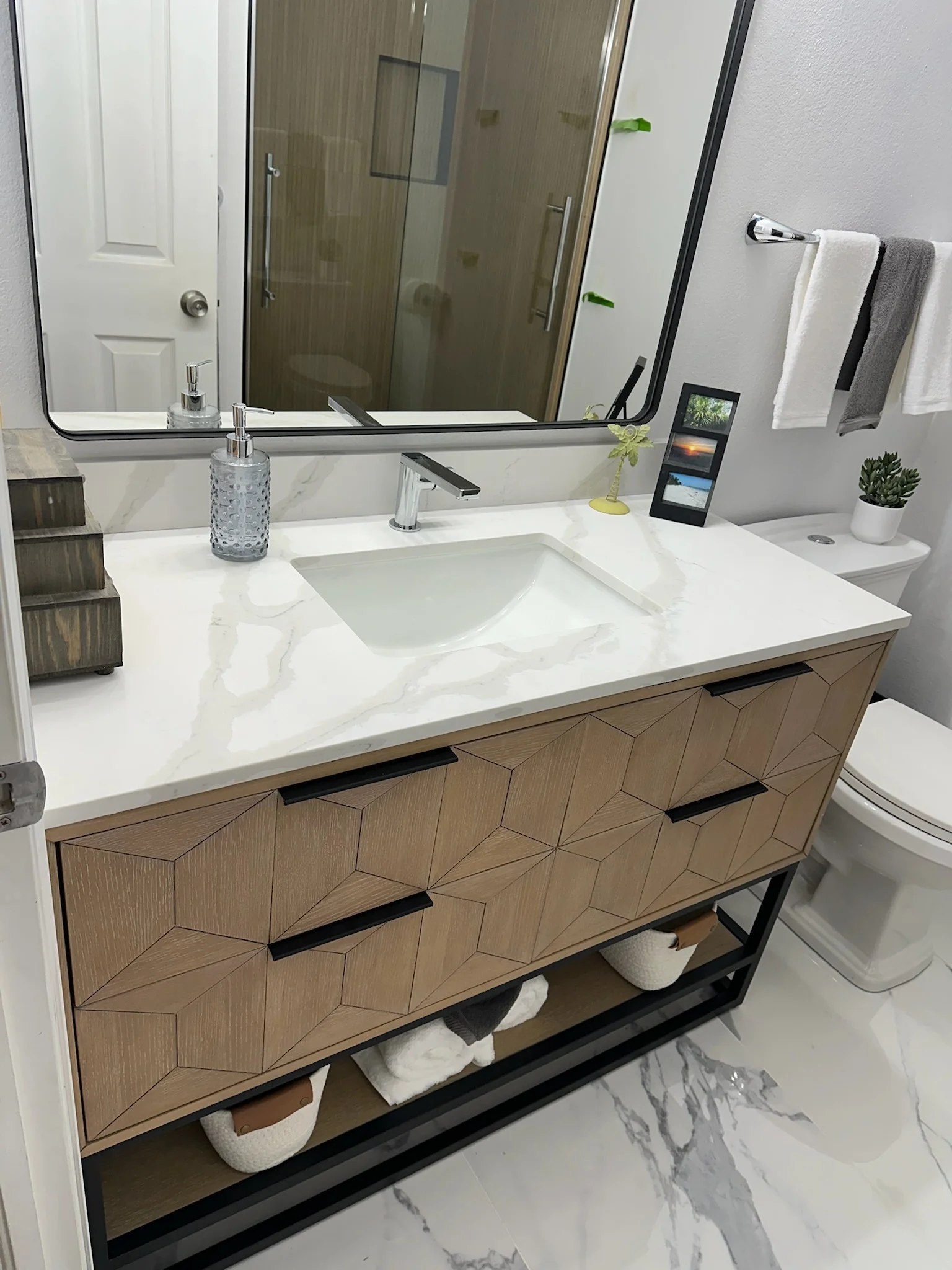 Wood vanity with geometric panels, white marble countertop, integrated sink, and framed mirror in modern bathroom