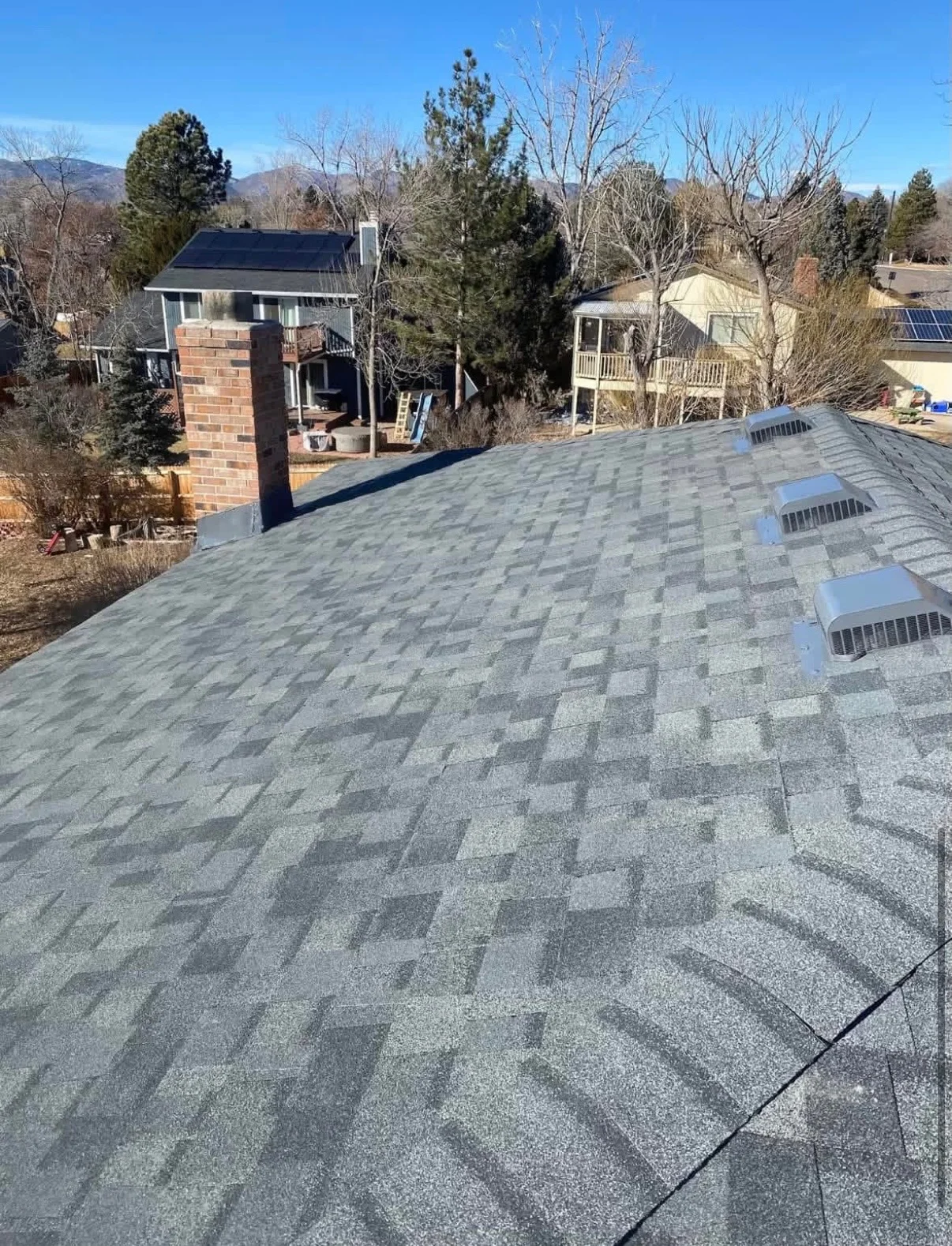 Gray architectural shingles with roof vents and brick chimney flashing