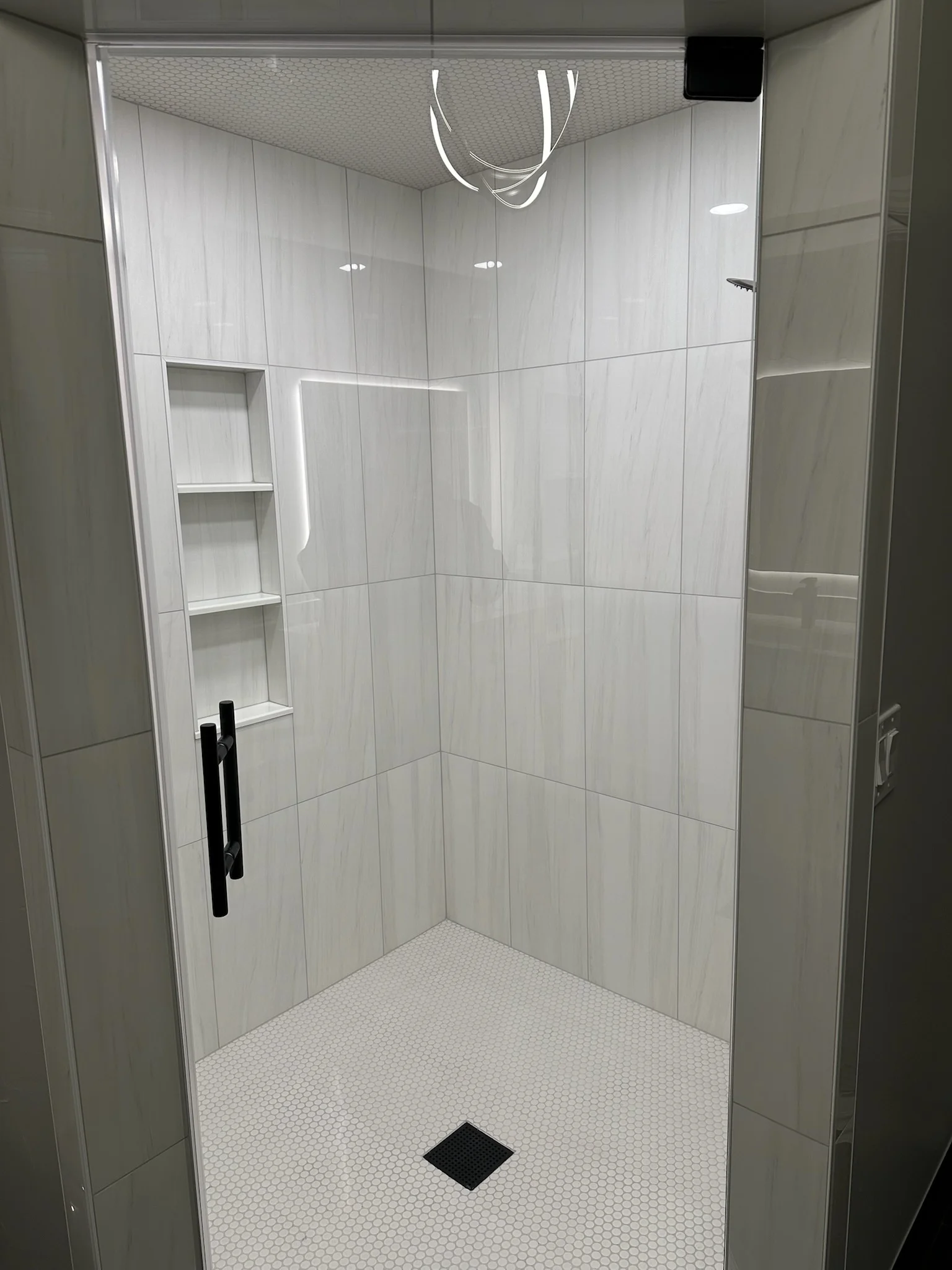 Walk-in shower with white wood-grain tile walls, built-in niches, mosaic floor, and frameless glass door