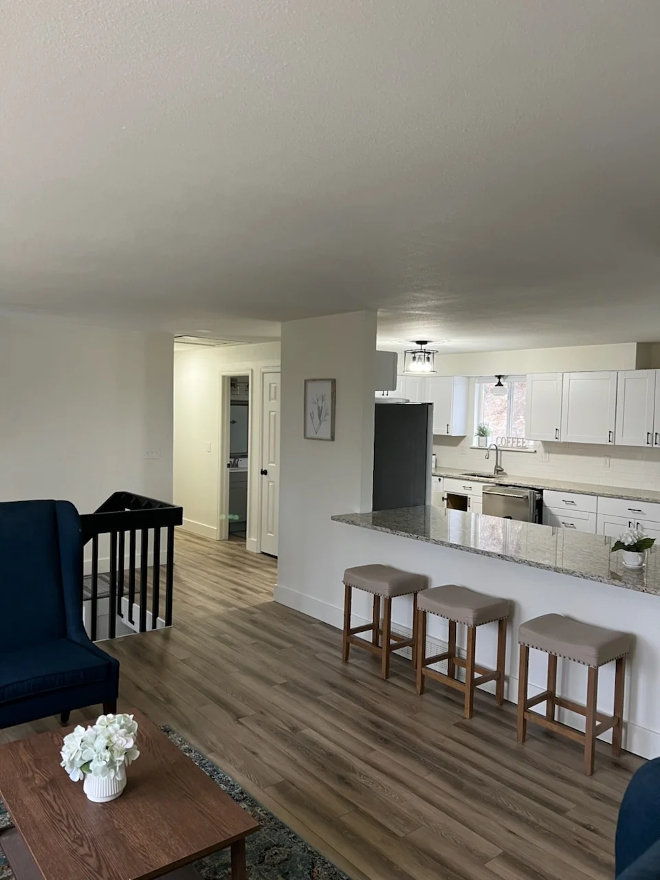 Open concept kitchen with white cabinets, granite island, vinyl plank flooring, and living room seating