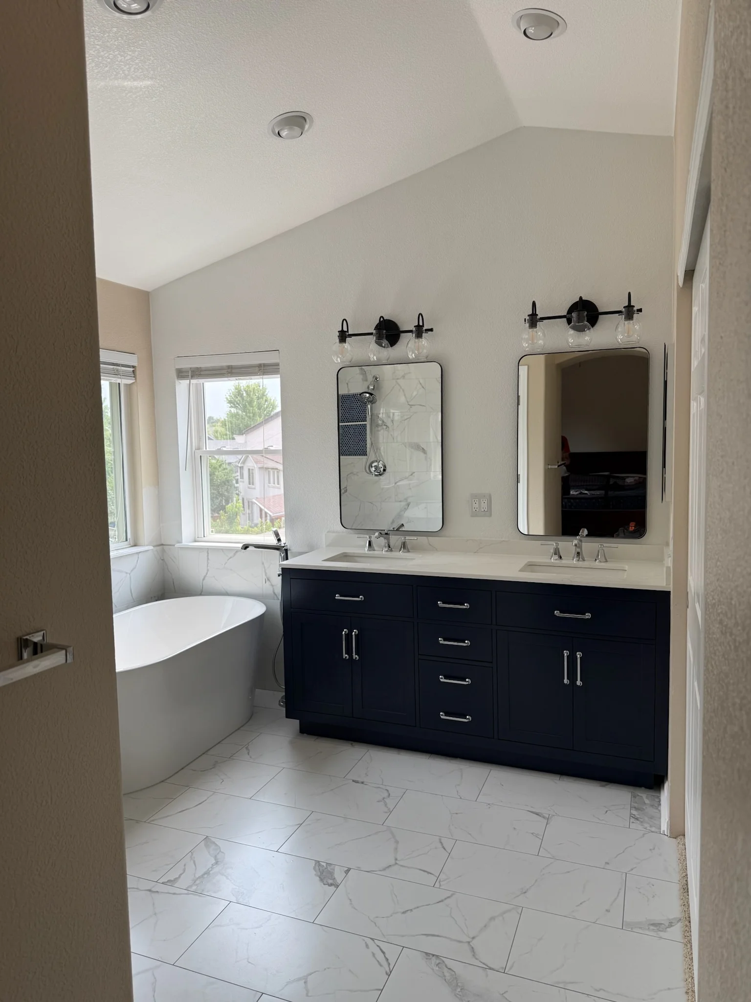 Master bathroom with freestanding tub, dual vanity, marble tile flooring, and black fixtures
