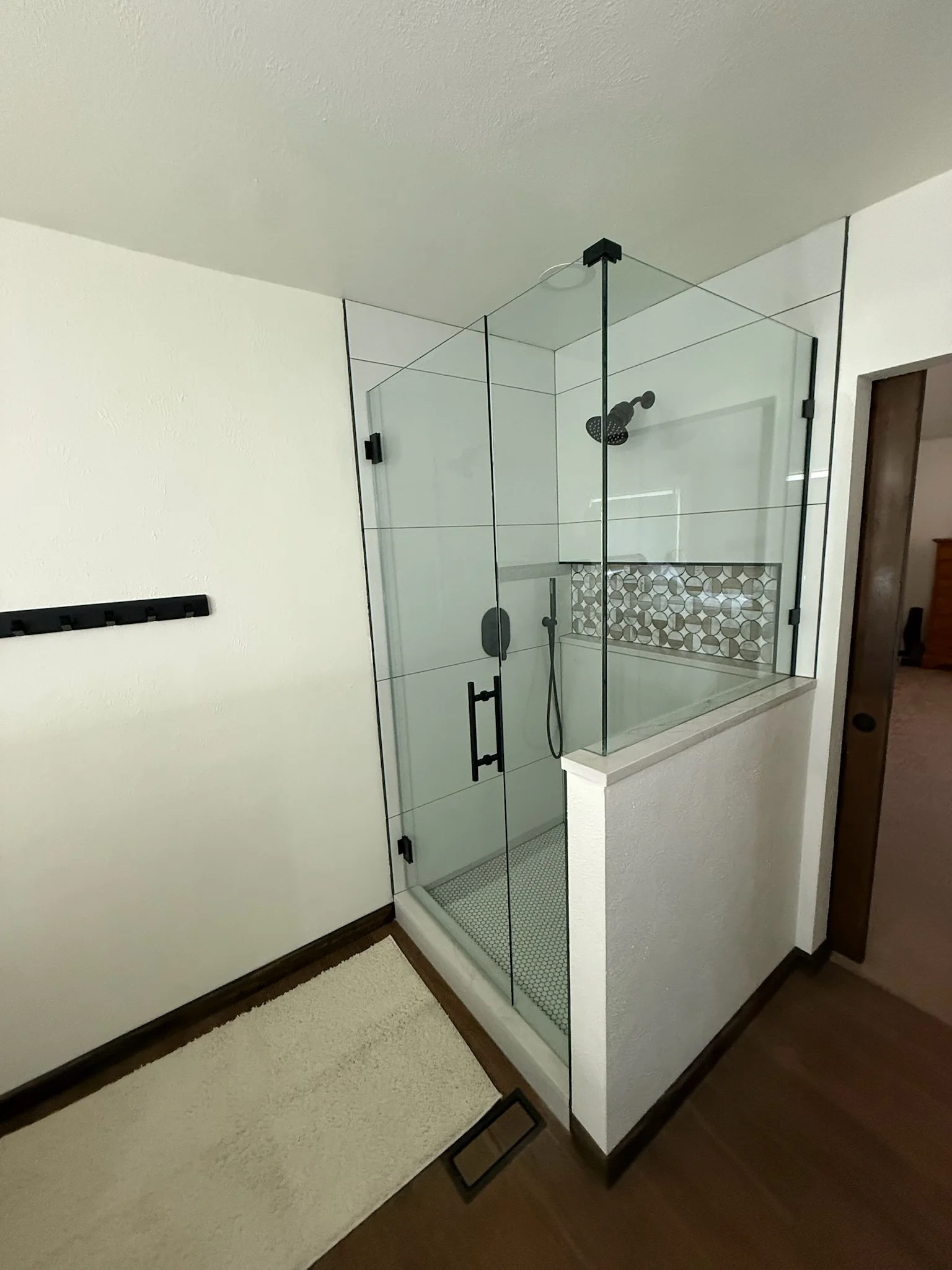 Frameless glass shower enclosure with black hardware, geometric tile accent, and rainfall showerhead