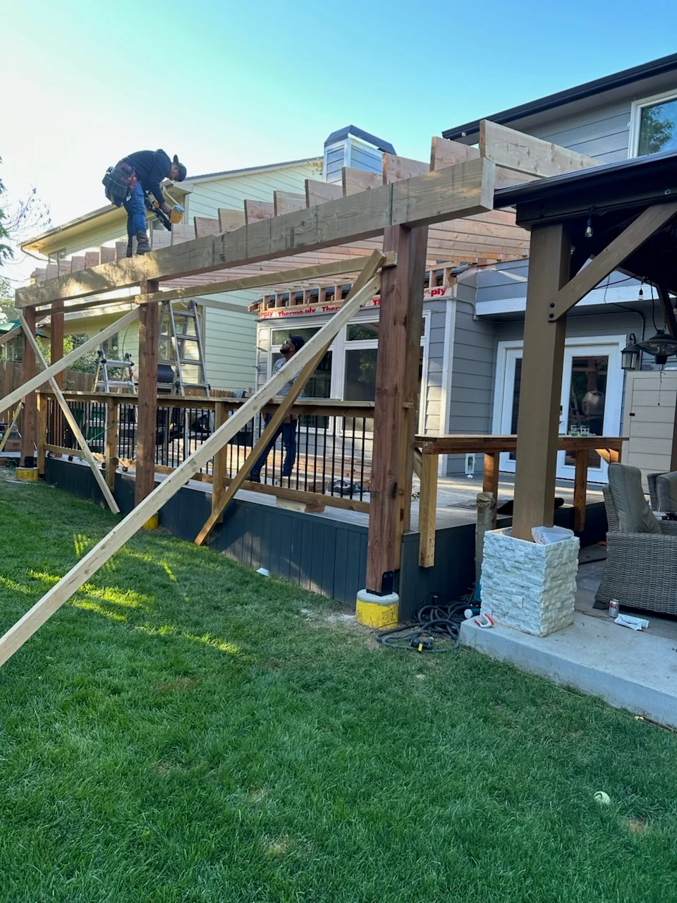 Two-level wood deck with pergola, metal railings, and composite decking under construction