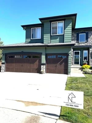 Two-story modern home with green siding, stone base, and double garage in Aurora