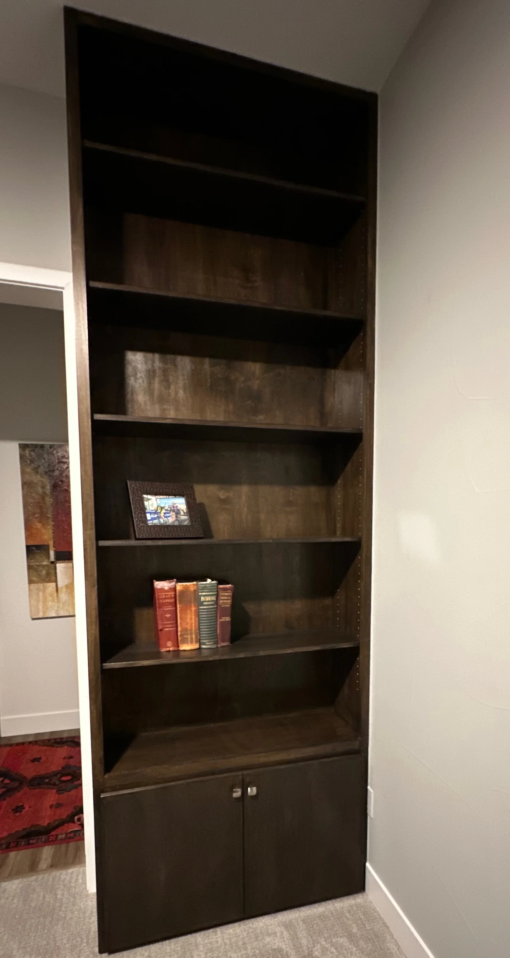 Dark wood built-in shelving unit with seven open shelves and lower cabinet storage doors