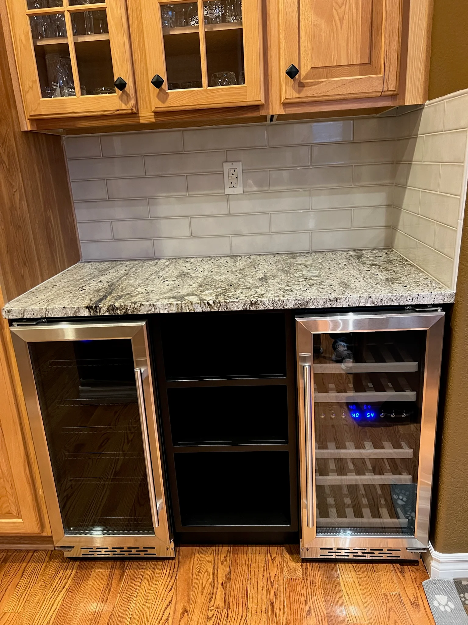 Granite countertop wet bar with stainless steel beverage coolers, subway tile backsplash, and wood cabinetry