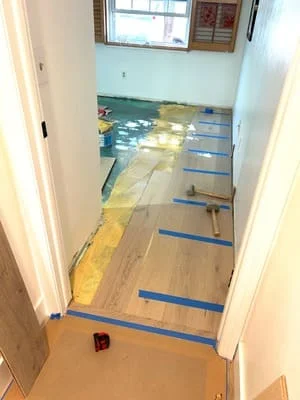 Hardwood floor installation in progress with blue protective tape and new wood planks