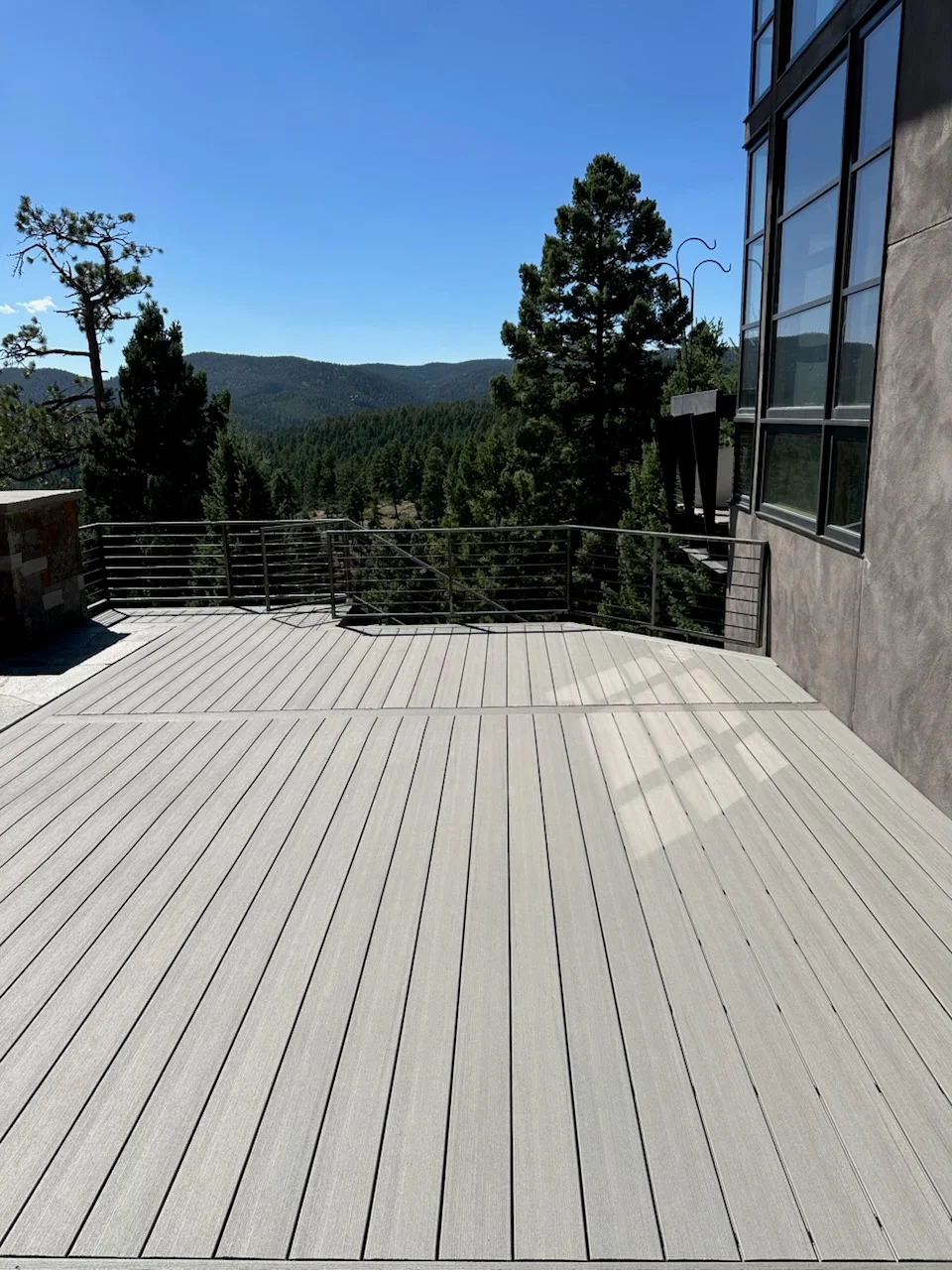 Light gray composite deck with cable railing overlooking forested mountain landscape